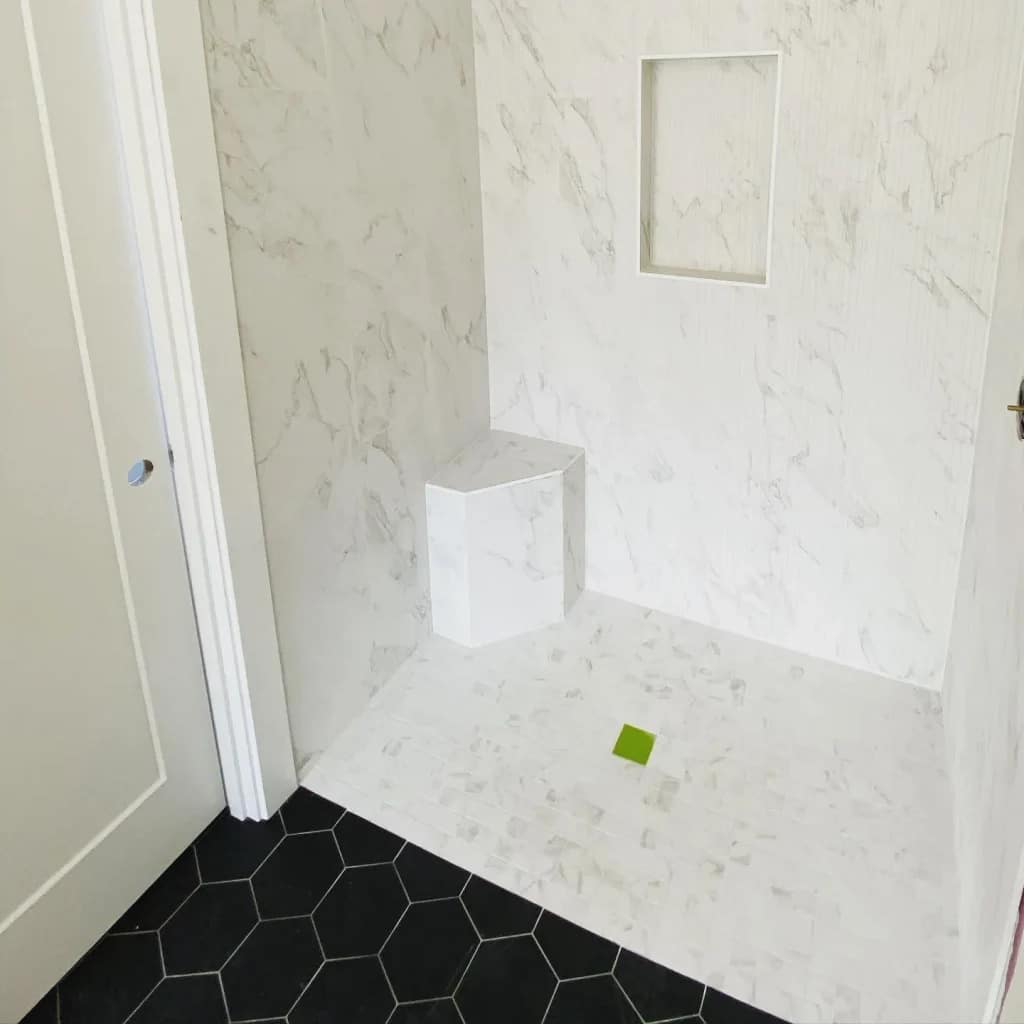 Shower space featuring white marble tile walls, a built-in niche, and a contrasting black hexagonal tile floor, showcasing tile installation craftsmanship by NW Tile & Flooring in Salem, Oregon.