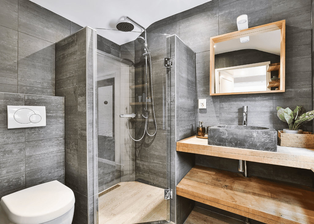 Modern bathroom with glass shower, dark tiled walls, wooden vanity, stone sink, and decorative plants, showcasing tile and flooring design for remodeling in Keizer, Oregon.