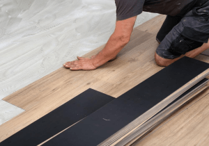 Person installing vinyl plank flooring over a subfloor, showcasing the flooring materials and installation process relevant to bathroom renovations.