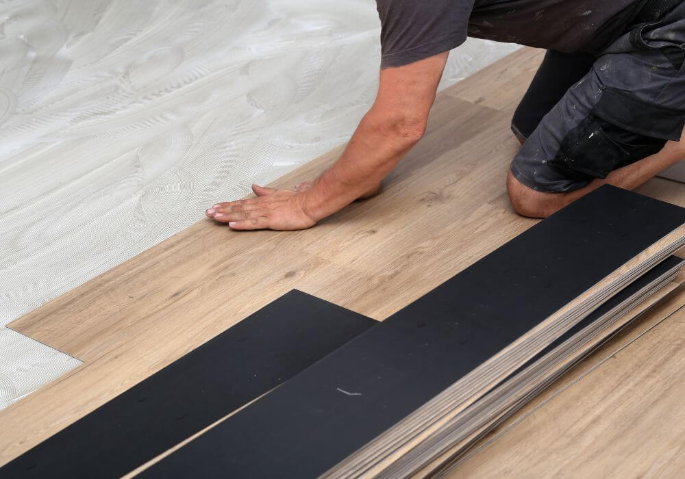 Person installing vinyl plank flooring, showcasing craftsmanship and attention to detail, with planks arranged and partially laid on the floor.