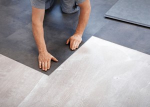 Person installing sheet vinyl flooring, showcasing installation process and material texture in home renovation context.