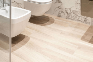 Bathroom floor featuring light wood-look tile, complemented by modern fixtures and marble wall accents, illustrating stylish and durable flooring options for bathroom design.