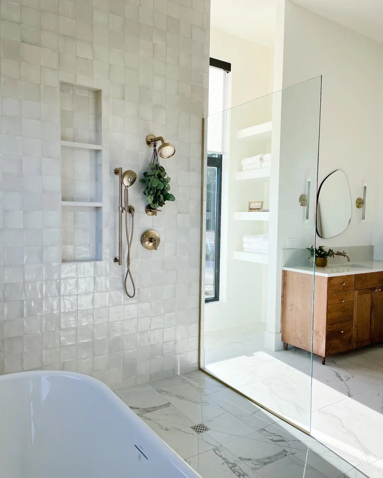Modern bathroom with white tiled walls, a glass shower enclosure, brass fixtures, and a freestanding bathtub, highlighting a sleek and stylish design ideal for laminate flooring installation.