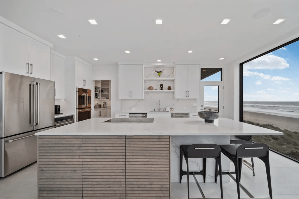 Modern kitchen featuring quartz countertops, sleek cabinetry, and large windows showcasing a beachside view, designed for luxury and functionality.